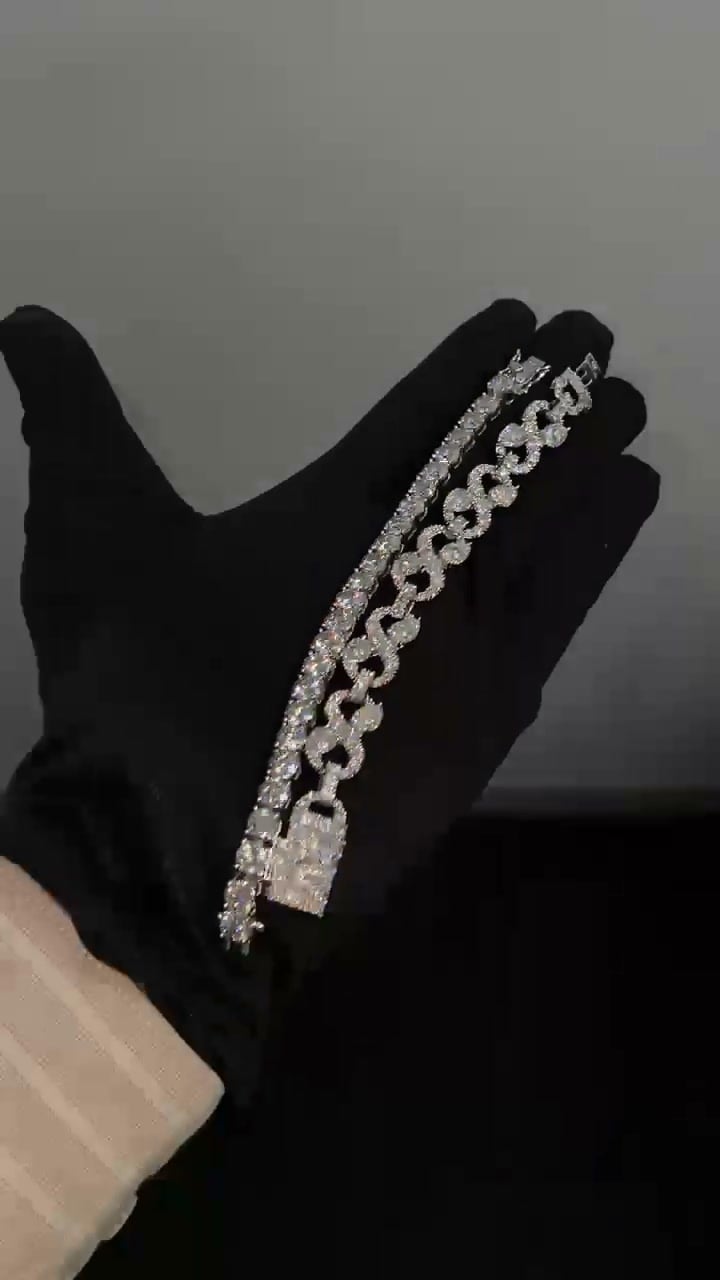 Stone-set open-link bracelet with round accents and a rectangular clasp, beside a separate tennis bracelet on a black glove.