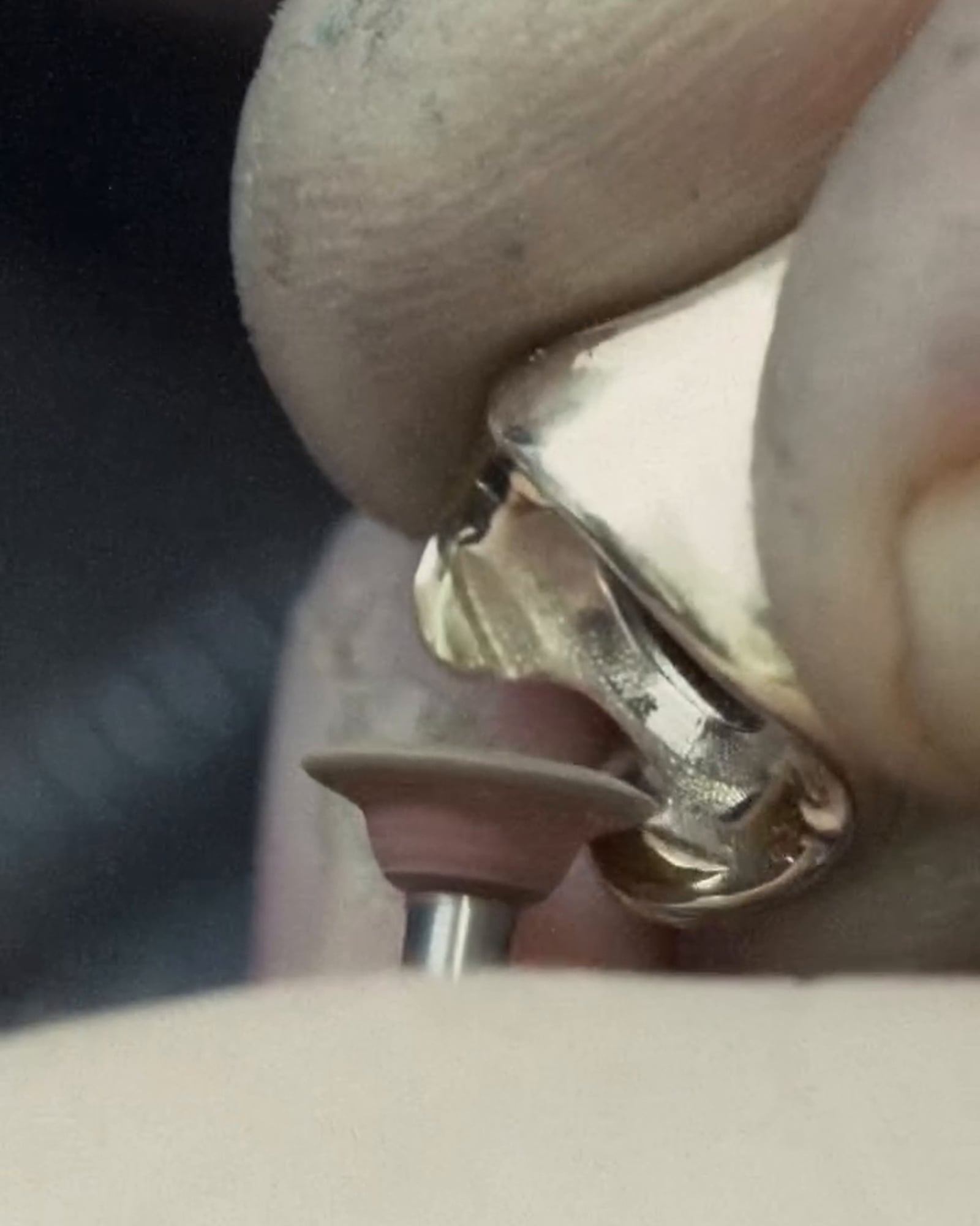 Fingers hold a gold-tone ring as a small rotary finishing wheel meets the inner surface of its band.