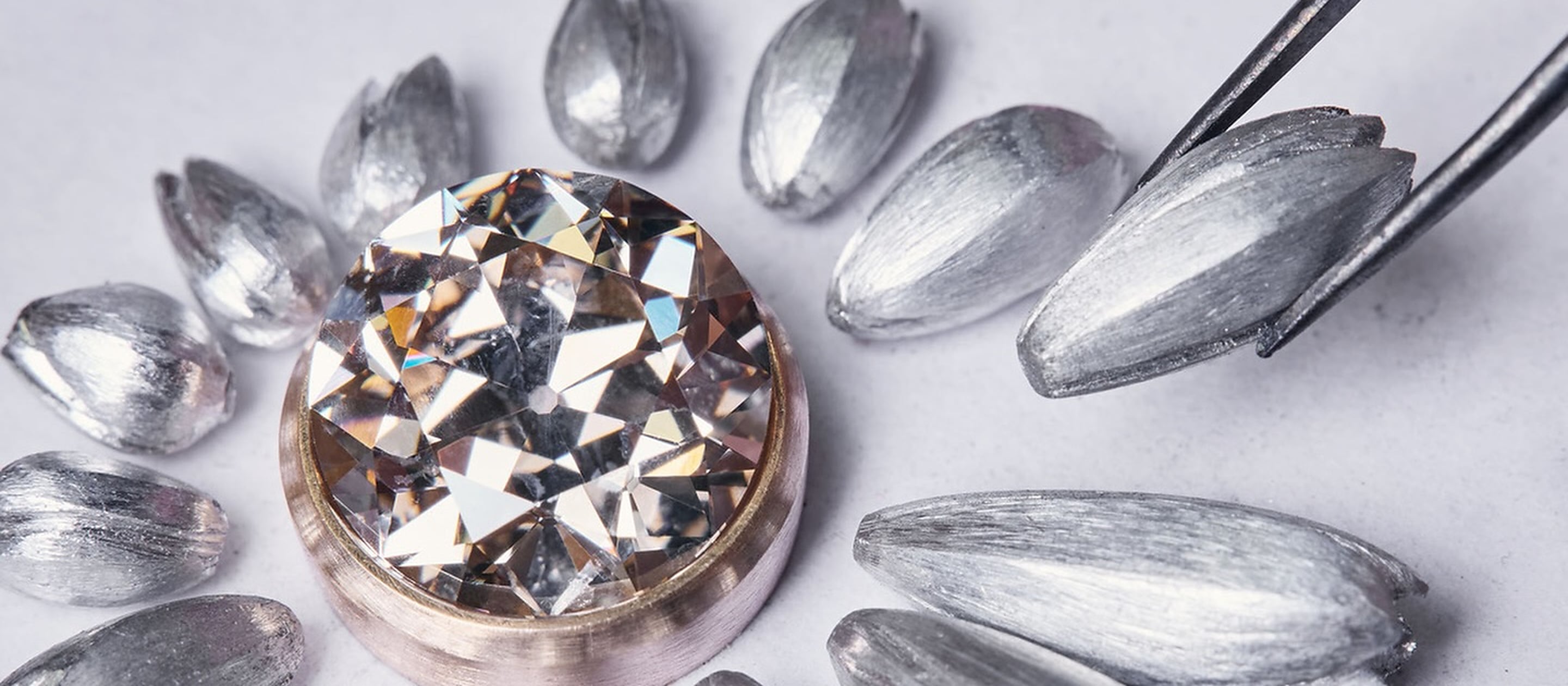 A clear faceted gemstone in a gold-tone setting on a drawn jewelry study, beside precision tweezers.