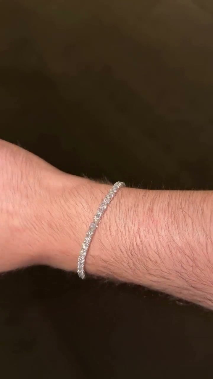Silver-tone tennis bracelet with a continuous line of round settings worn on a wrist against a dark background.