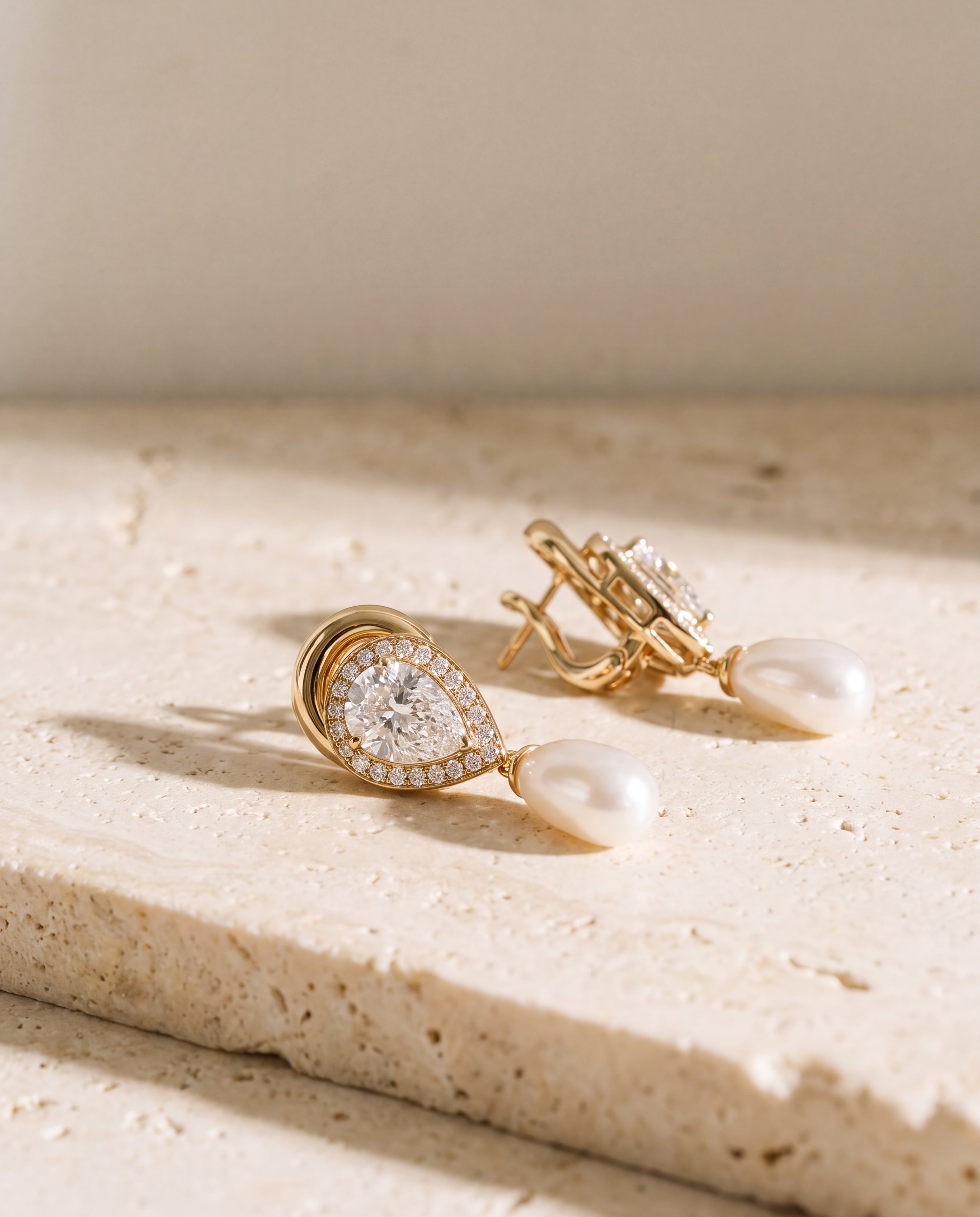 A pair of gold-tone earrings with clear stones and white drops on pale stone.