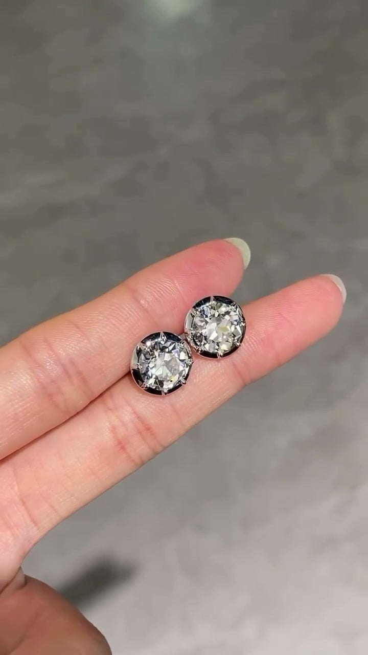 Pair of round faceted stud earrings in compact silver-tone settings balanced on fingers.