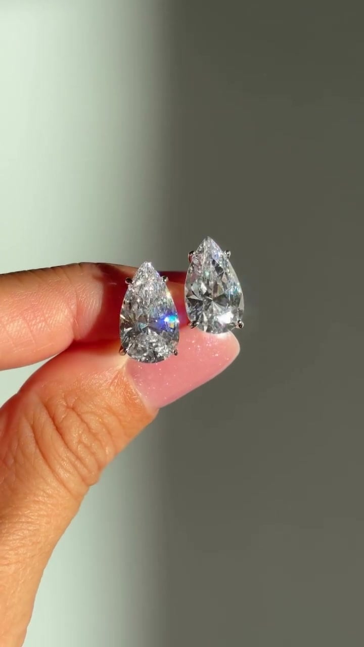 Pair of pear-shaped stud earrings with visible prongs, held upright between fingers.