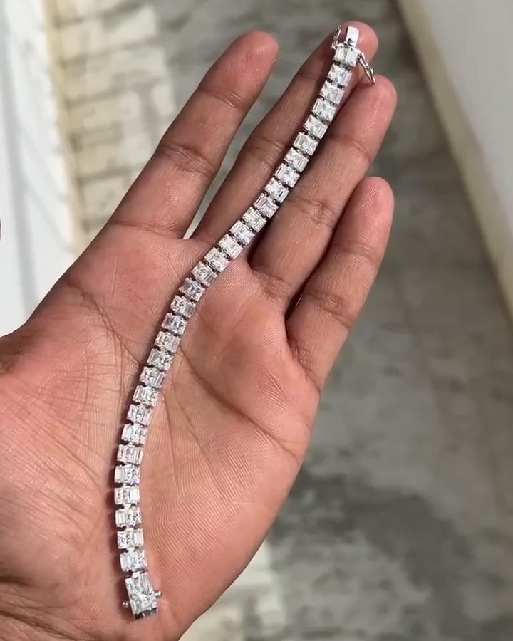 Single-row bracelet with square-faced stone settings and visible clasp hardware resting across a palm.