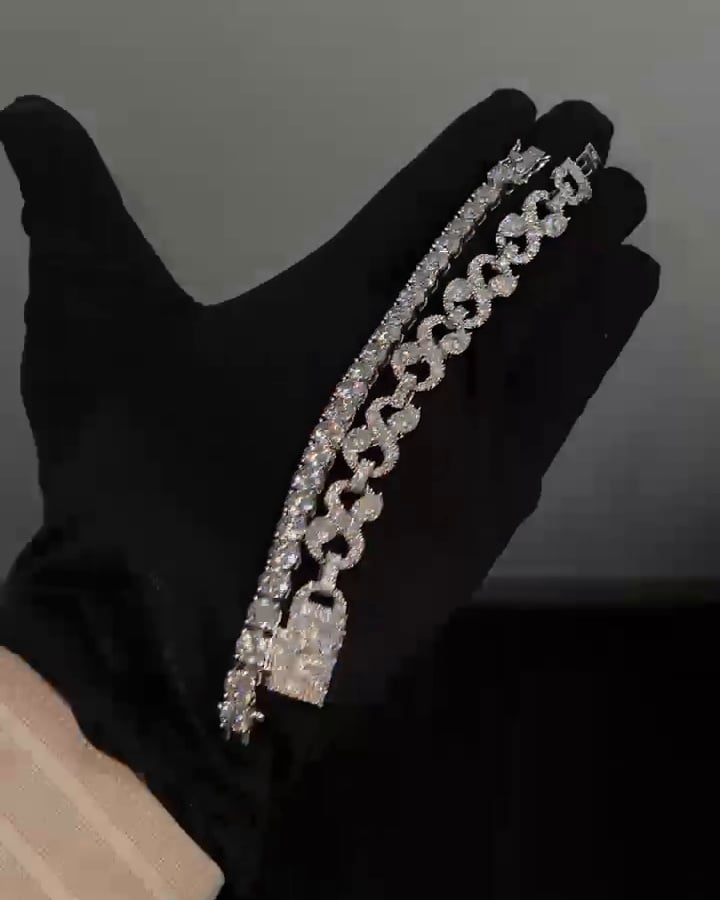 Stone-set open-link bracelet with round accents and a rectangular clasp, beside a separate tennis bracelet on a black glove.