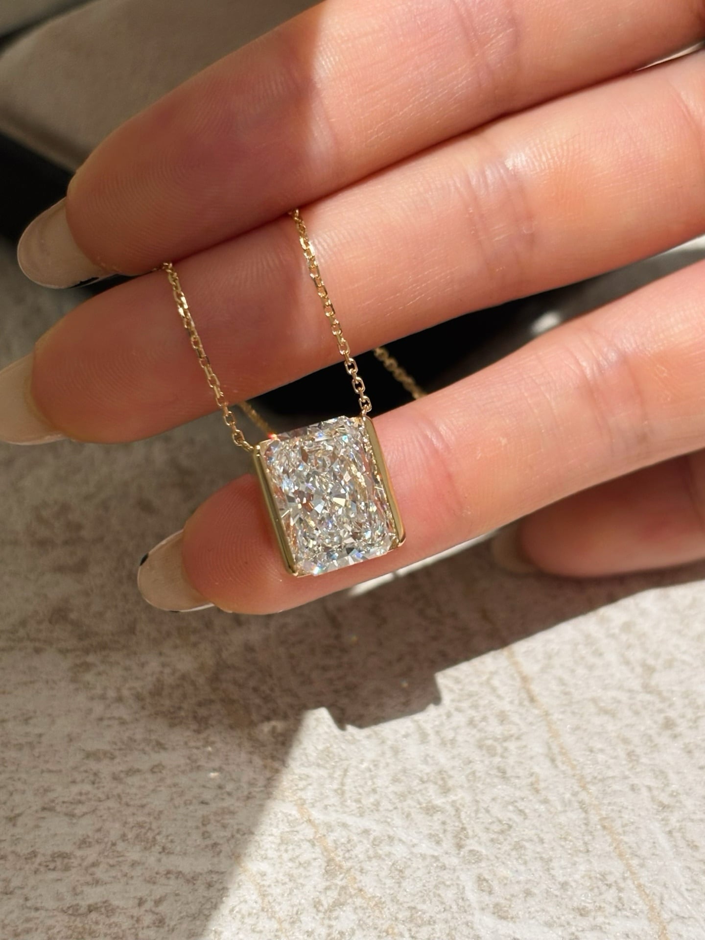 Rectangular faceted pendant with yellow-tone side rails and two chain attachments, held against fingers in daylight.