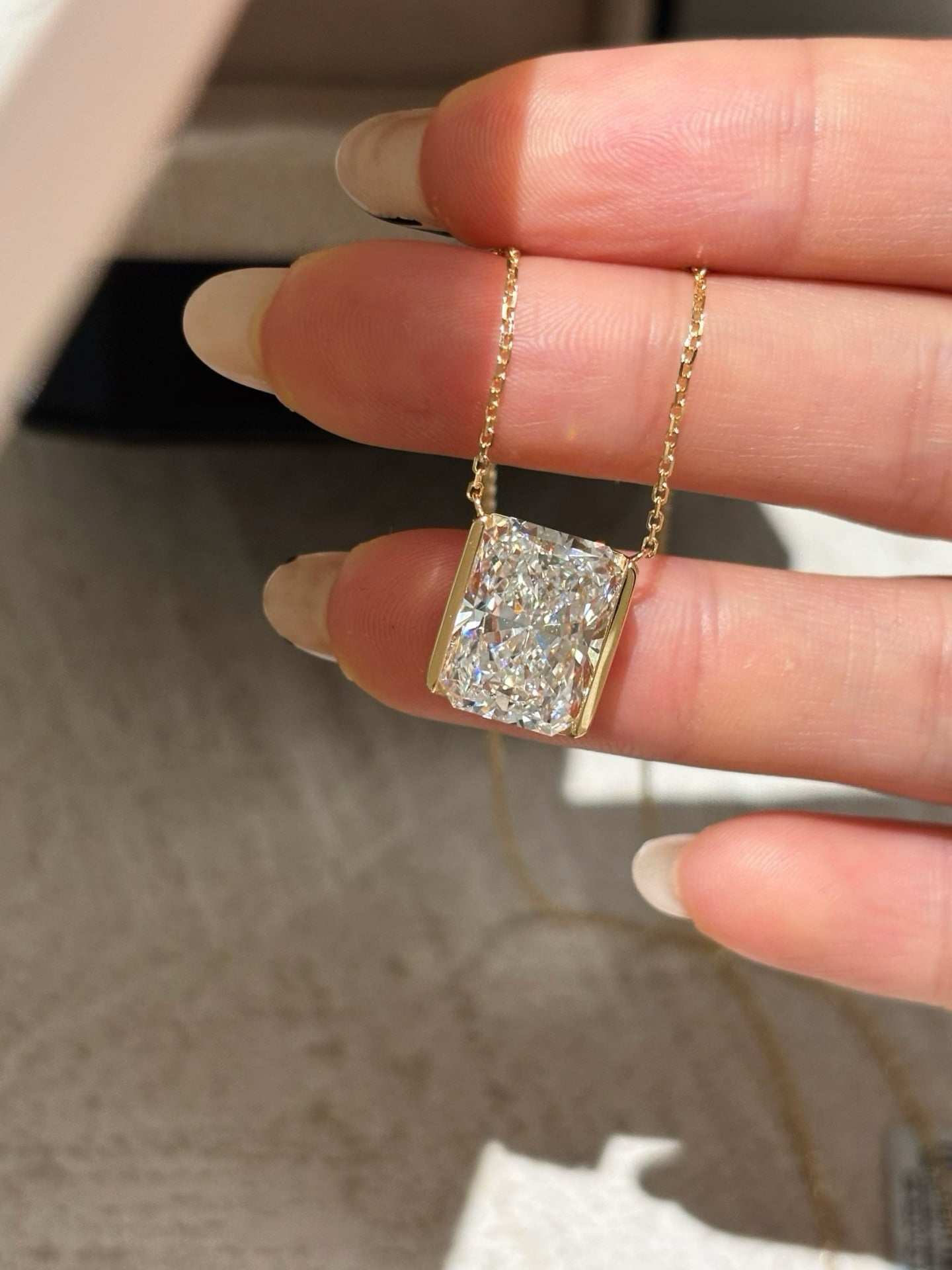 Alternate front view of the same rectangular pendant with yellow-tone side rails suspended across fingers.