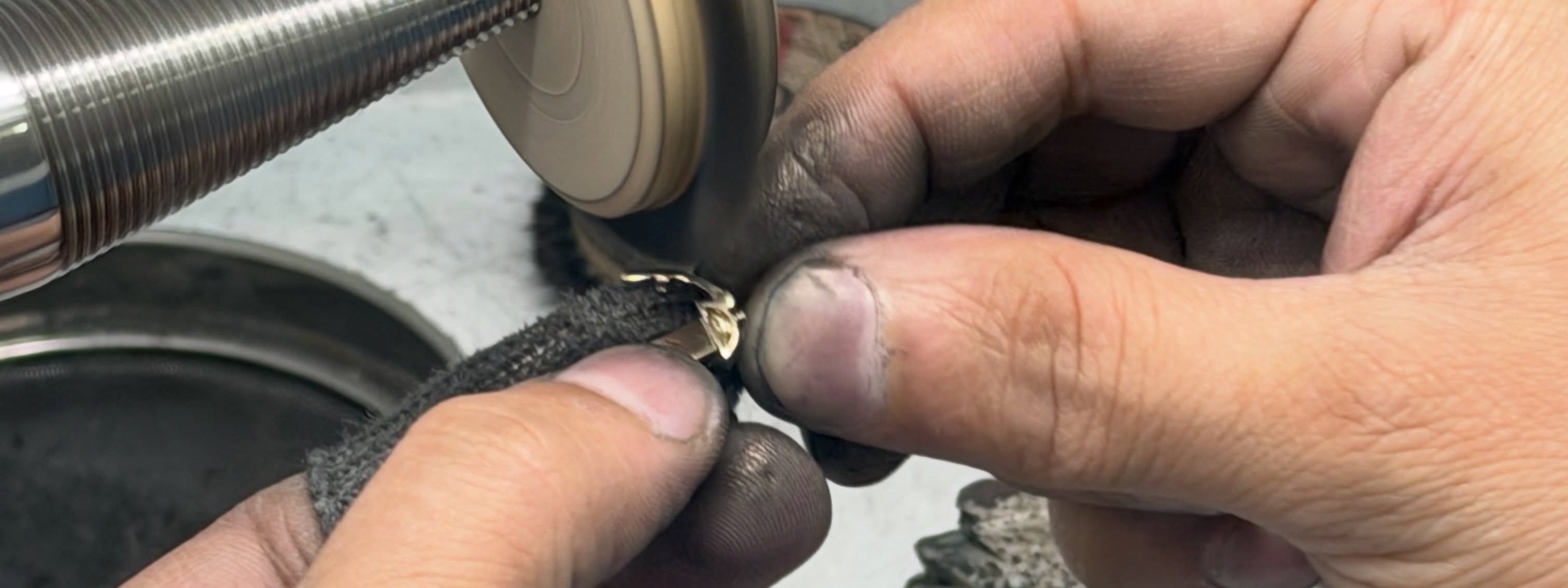 Hands hold a gold-tone jewelry piece against a rotating finishing wheel.