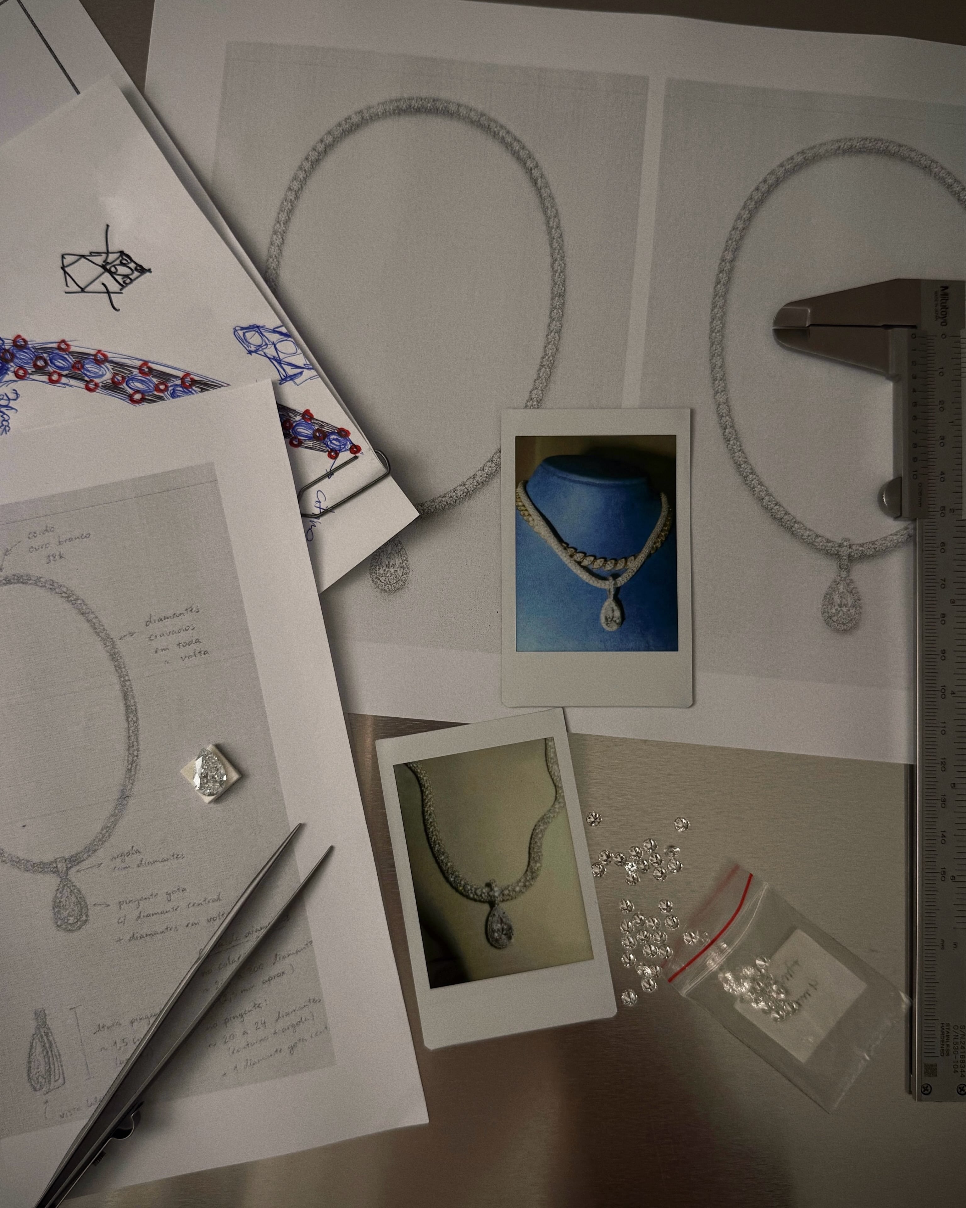 Jewelry sketches, necklace studies, loose stones and small collection photographs arranged on a work surface.